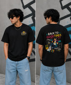 Person wearing a black t-shirt with colorful graphics and text, standing against a gray wall.