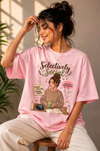 Woman wearing a pink t-shirt with a graphic design sitting on a stool.