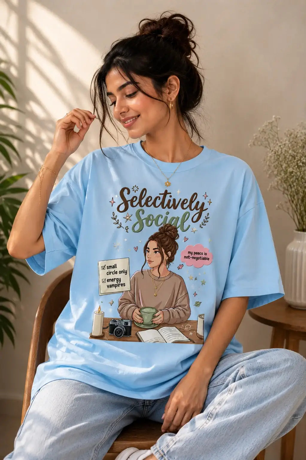 Woman wearing a light blue t-shirt with a graphic design sitting in a room.