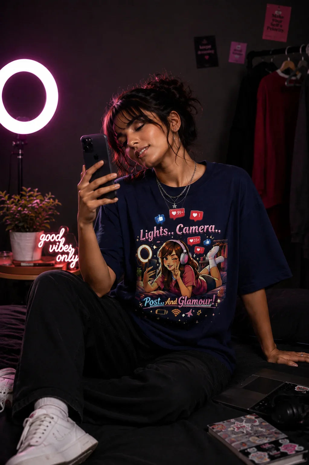 Person wearing a graphic t-shirt sitting in a room with a ring light and laptop.
