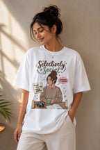 Woman wearing a white t-shirt with a graphic design and text, standing against a beige wall.