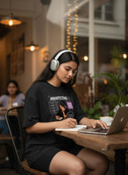 Black t-shirt with "Manifesting Dream Believe Work Achieve" graphic. Woman with headphones working on laptop.