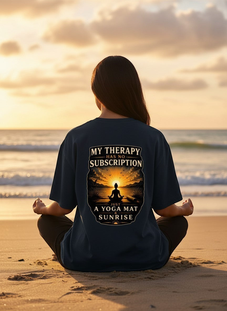 vcreate4uhub.co.in black t-shirt with "My Therapy Has No Subscription Just A Yoga Mat & Sunrise" graphic on back. Model meditating on beach.